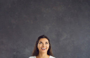 Smiling young Hispanic woman on black studio background look up at blank empty copy space. Happy...