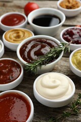 Different tasty sauces in bowls, rosemary and thyme on wooden table, closeup