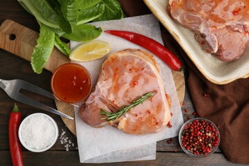 Flat lay composition with raw marinated meat, lemon, rosemary and spices on wooden table