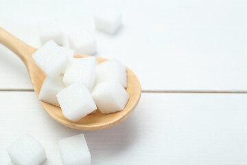 Many sugar cubes and wooden spoon on white table, closeup. Space for text