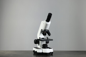 Modern medical microscope on grey table against light background