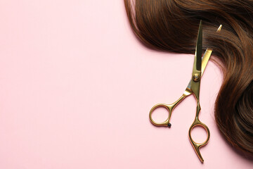 Professional hairdresser scissors with brown hair strand on pink background, top view. Space for...
