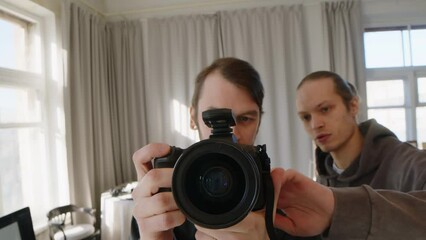 POV shot of Caucasian male expert photographer helping young assistant to adjust settings on professional digital camera while shooting in bright studio at daytime