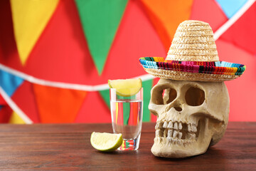 Human scull with Mexican sombrero hat and tequila on wooden table. Space for text