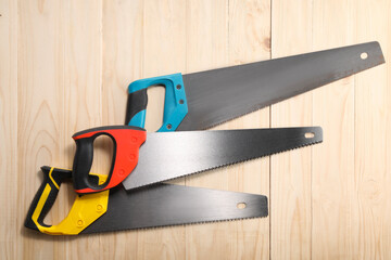 Saws with colorful handles on wooden background, flat lay