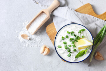 Delicious yogurt with green onion in bowl, garlic, salt and lemon on light textured table, flat lay