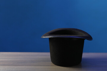Magician's hat on wooden table against blue background, space for text