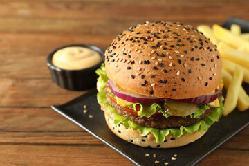 Burger with delicious patty, french fries and sauce on wooden table, closeup