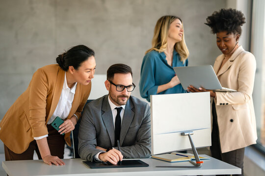 Senior business manager talking with experienced colleague while using computer in office.