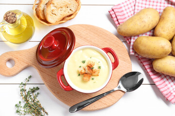 Tasty potato soup with croutons and rosemary in ceramic pot served on white wooden table, flat lay