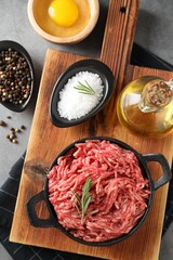 Raw ground meat in bowl, spices, egg and oil on grey table, flat lay