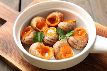 Delicious cooked snails with parsley in bowl on table, closeup