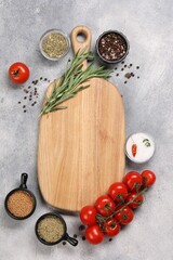Wooden cutting board surrounded by spices and tomatoes on grey textured table, flat lay. Space for text
