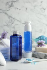 Spa composition. Bottles of cosmetic products, sea salt, stones, soap and flowers on white table