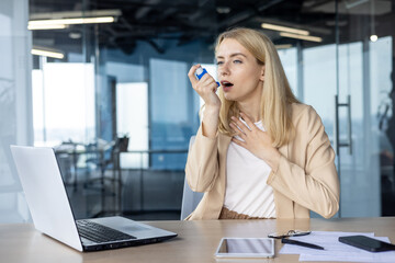 Businesswoman using an asthma inhaler in a modern office