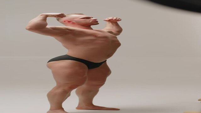 Vertical shot of Caucasian young handsome man with muscles posing with bare torso for camera having studio photoshoot with professional photo production crew