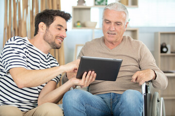 cheerful disabled man near handsome son looking at tablet