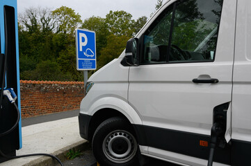 An electric van is charging at a photovoltaic station in a car park. A sign reads "Reserved for recharging electric vehicles".