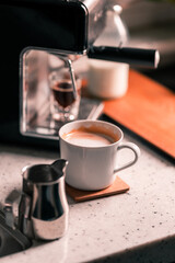 A glass of caffe latte with home coffee machine with a shot glass of espresso in the background