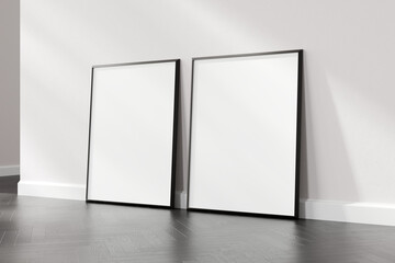 Two empty picture frames resting on a wooden floor against a white wall, suitable for art display...