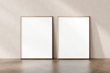 Two empty picture frames leaning against a plain wall on a herringbone parquet floor, awaiting...