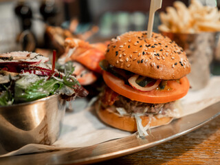 A burger with a tomato and lettuce on it is on a plate. A salad is also on the plate