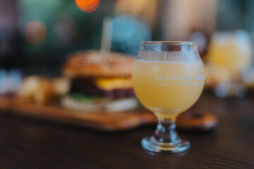 A glass of beer sits on a table next to a hamburger