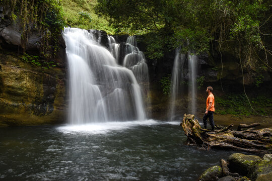 Man standing on a log in front of a waterfall 