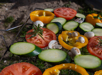 Colorful fresh vegetables prepared slices are laid out on a grill for grilling. Tomatoes, zucchini, peppers, and mushrooms.