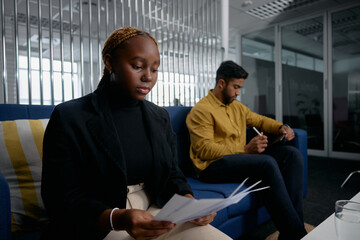Two multiracial young business people in businesswear reading papers and using digital tablet in office