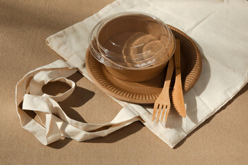 A set of paper utensils and wooden cutlery in fabric bag on a brown background. Eco friendly, zero...
