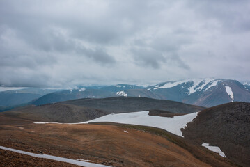 Dark overcast landscape with high pass, wide glacier on stony hill slope and snowy mountain range...