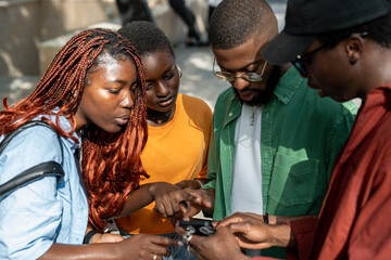 Interested focused four african american students looking online information on smartphone prepare...