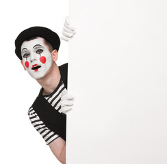 Funny mime artist peeking out of blank poster on white background