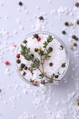 Salt with peppercorns and thyme in bowl on light table, top view