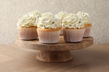 Tasty vanilla cupcakes with cream on wooden table