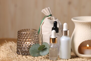 Different aromatherapy products, burning candles and eucalyptus leaves on table, closeup