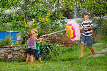 Siblings boys and girl having fun with water spray in garden