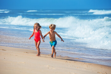 A boy and girl joyfully running on sandy beach beside the waves