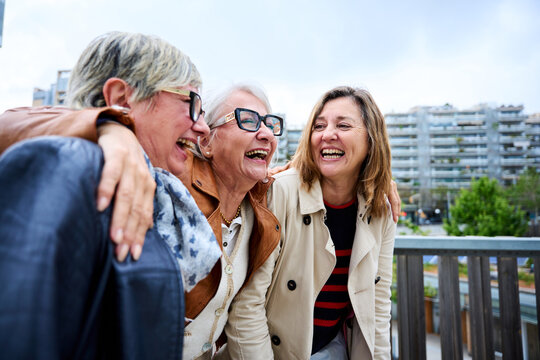 Group of three mature caucasian women enjoying embracing walk together laughing outdoor. Senior female friends having fun hugging strolling happy in the urban city street. Elderly people enjoying