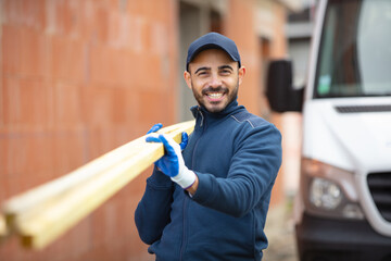 young carpenter carrying wood on shoulder at construction site