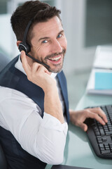 smiling man wearing headset and typing on computer keyboard
