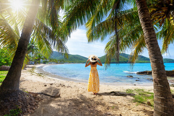 A woman in a yellow summer dress stands on a tropical paradise beach at the Caribbean islands of...