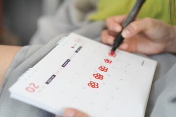 Young woman marking days of menstruation on the calendar