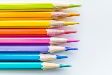 Fototapeta premium Office for school classes or art classes. Colored pencils arranged in a row on a white background in close-up.