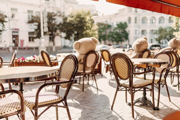 A restaurant with a lot of chairs and tables. There are two teddy bears on the tables.