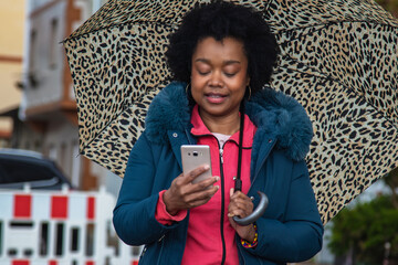 afro woman on the street with umbrella using mobile phone