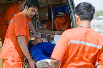 Group of paramedic or emergency medical technician (EMT) in an orange uniform places a neck and head accident victim on a bed in an ambulance. Urgent assistance during road accident.