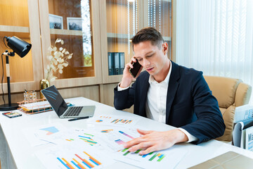 Caucasian business manager using phone to call customer while analyzing the sales report from marketing team for business income and financial management usage
