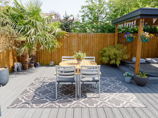 Naklejka premium Minimalistic English modern garden with table and chairs. Sunny summers day with green plants and decking on the patio